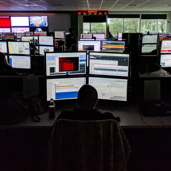 A network operations agent working at a bank of a dozen monitors in a dim call center, conducting contextual research into the tools agents use every day.