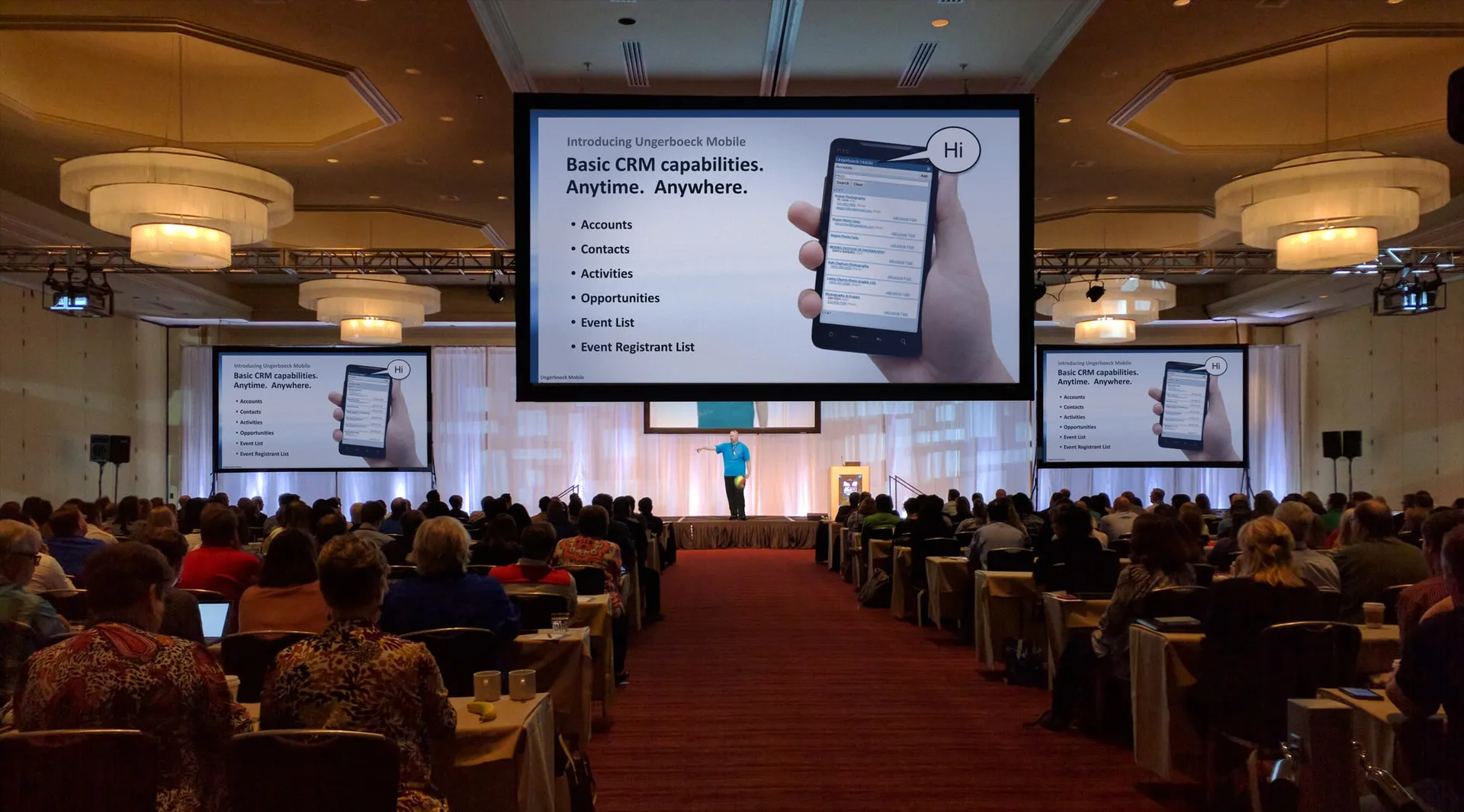 Wayne presenting Ungerboeck Mobile on stage at a conference, with the “Introducing Ungerboeck Mobile” slide displayed on giant screens above rows of seated attendees.